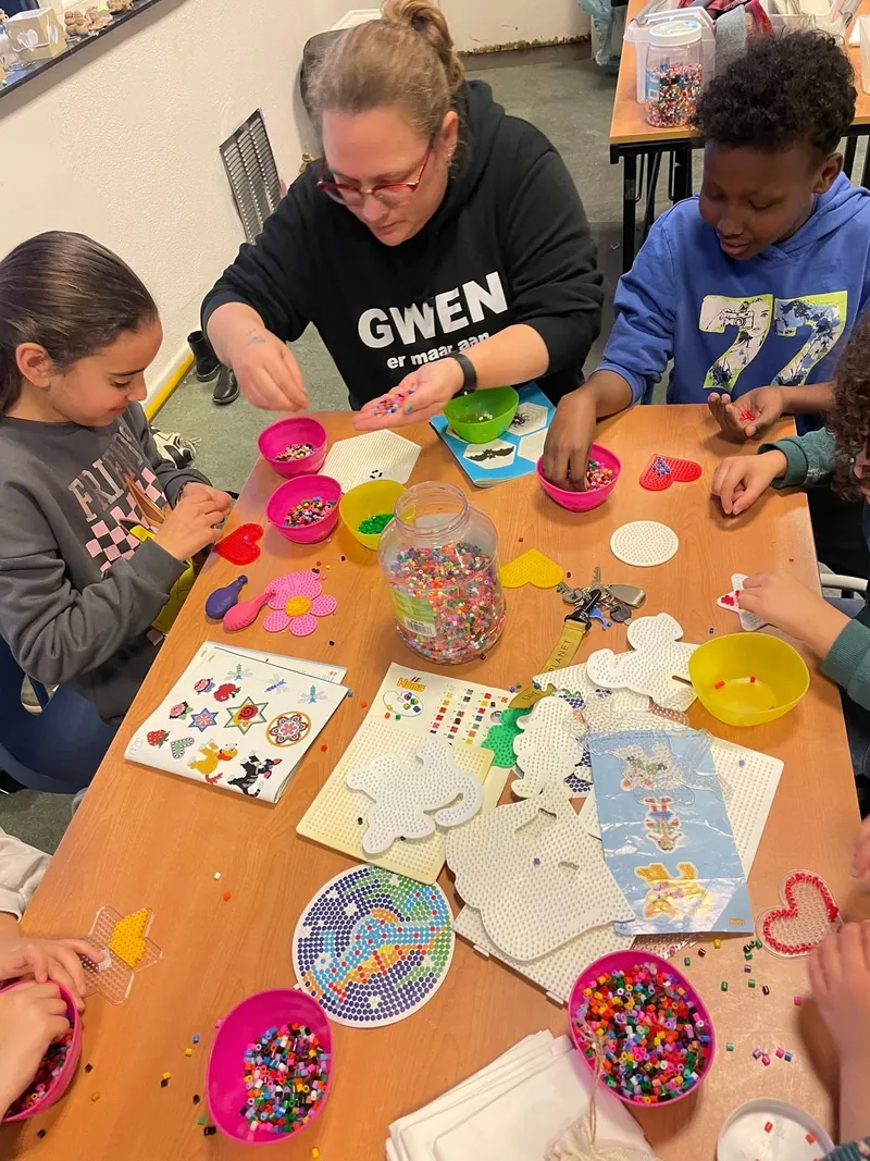 Kinderen knutselen met strijkkralen aan een grote tafel